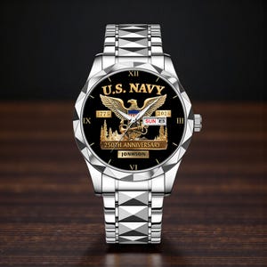 May include: A silver wristwatch with a black face featuring the text "U.S. NAVY" and an eagle emblem. The watch face also displays "1775" and "2025", with "250TH ANNIVERSARY" and the name "JONHSON" below. The watch band is silver.
