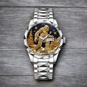 May include: Silver wristwatch with a detailed gold-colored Sasquatch design on the watch face. The watch face also features gold trees, stars, and the name "JAMES". The date is displayed as "SUN 8".