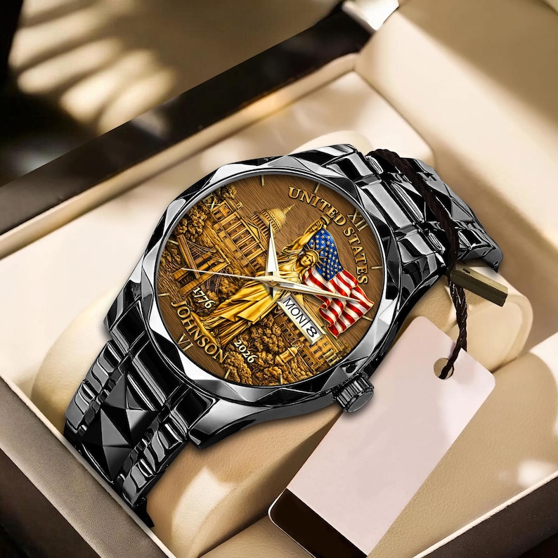 Peut inclure: Une montre-bracelet avec un cadran marron repr&eacute;sentant en or le Capitole des &Eacute;tats-Unis, un drapeau am&eacute;ricain et le texte "UNITED STATES" et "JOHNSON VI 2026". La montre a un bracelet en m&eacute;tal noir et est pr&eacute;sent&eacute;e dans une bo&icirc;te.