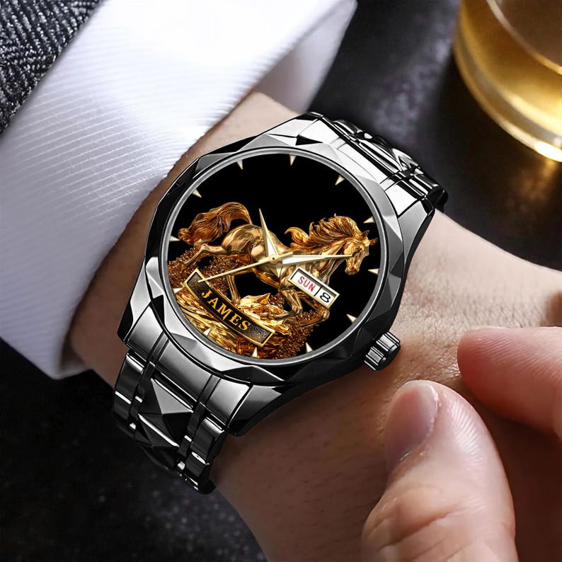 May include: A silver-toned wristwatch with a black face featuring a gold-colored horse design. The watch face displays the day and date. The band is made of silver-toned metal. The watch has the name "JAMES" on the face.