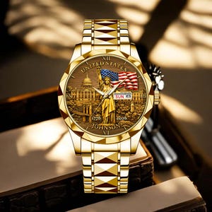 Peut inclure: Montre-bracelet dor&eacute;e avec un cadran d&eacute;taill&eacute; repr&eacute;sentant la Statue de la Libert&eacute;, un drapeau am&eacute;ricain et l'inscription "UNITED STATES". Le bracelet de la montre pr&eacute;sente un motif g&eacute;om&eacute;trique. La date est affich&eacute;e comme "SUN 8".