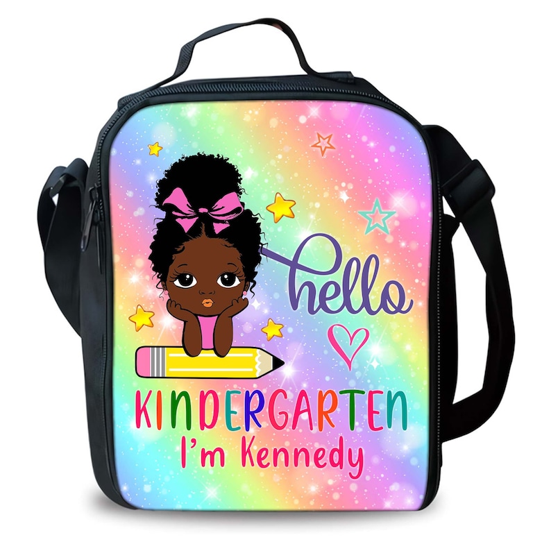 Peut inclure: Un sac &agrave; d&eacute;jeuner noir avec un fond arc-en-ciel et des paillettes. Une fille de dessin anim&eacute; avec un n&oelig;ud rose est assise sur un crayon jaune. Le texte dit "hello kindergarten I'm Kennedy".