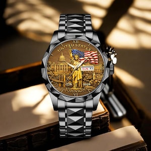 Peut inclure: Une montre-bracelet argent&eacute;e avec un cadran d&eacute;taill&eacute; repr&eacute;sentant la Statue de la Libert&eacute;, le drapeau am&eacute;ricain et le Capitole des &Eacute;tats-Unis. Le cadran affiche &eacute;galement la date. Le bracelet est &agrave; maillons g&eacute;om&eacute;triques.