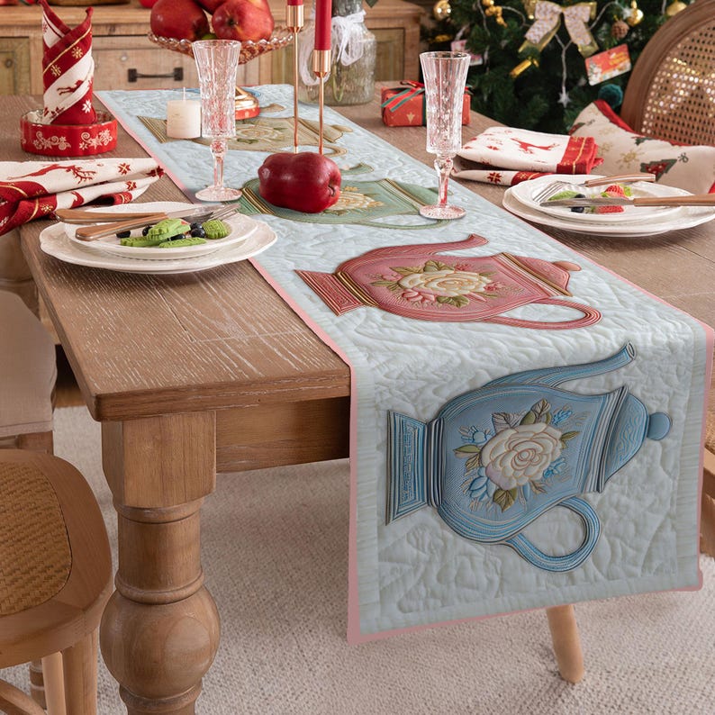 Pu&ograve; includere: Runner da tavolo trapuntato azzurro con bordi rosa, con teiere in rilievo rosa e blu con disegni floreali. Il runner &egrave; posto su un tavolo di legno apparecchiato per un pasto, con piatti, bicchieri e oggetti decorativi.