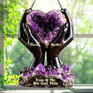 May include: A decorative heart-shaped amethyst geode held by two black hands. The geode is a deep purple color, and the hands are glossy. The base has the text "You & Me We Got This". The names "David" and "Sophia" are also visible.