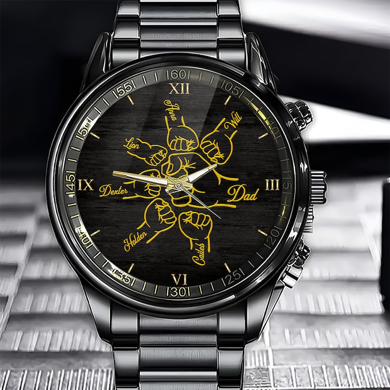 May include: Black wristwatch with a black face and gold Roman numeral hour markers. The watch face features a design of five fists with names written on each fist: Lion, Dexter, Holden, Caileb, and Dad. The names are written in gold.