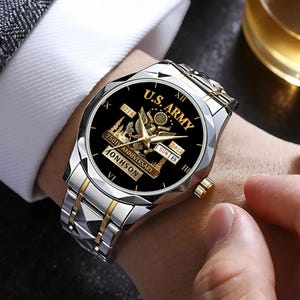 May include: A silver and gold wristwatch with a black face featuring the text "U.S. ARMY" and "250TH ANNIVERSARY". The watch has a date display and a silver and gold band. The watch is on a wrist.
