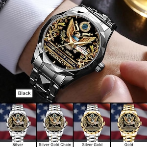 May include: A black wristwatch with a stainless steel band. The watch face features a gold eagle design, the text "UNITED STATES OF AMERICA", and the name "JOHNSON". The watch also displays the date "SUN 8" and the years "1776-2026".