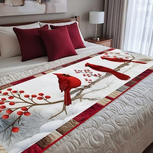 May include: A white bed runner featuring three red cardinal birds perched on branches with red berries. The runner has a red border and is placed on a bed with burgundy pillows and a white comforter. The artwork has a winter theme.