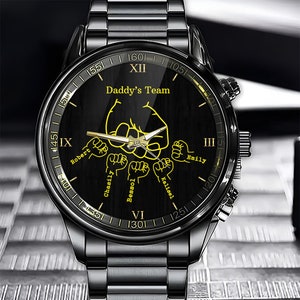 May include: Black wristwatch with a black face and gold accents. The face has the words "Daddy's Team" and the names "Robert", "Chasily", "Bessol", "Kalisel", and "Emily" around the edge.