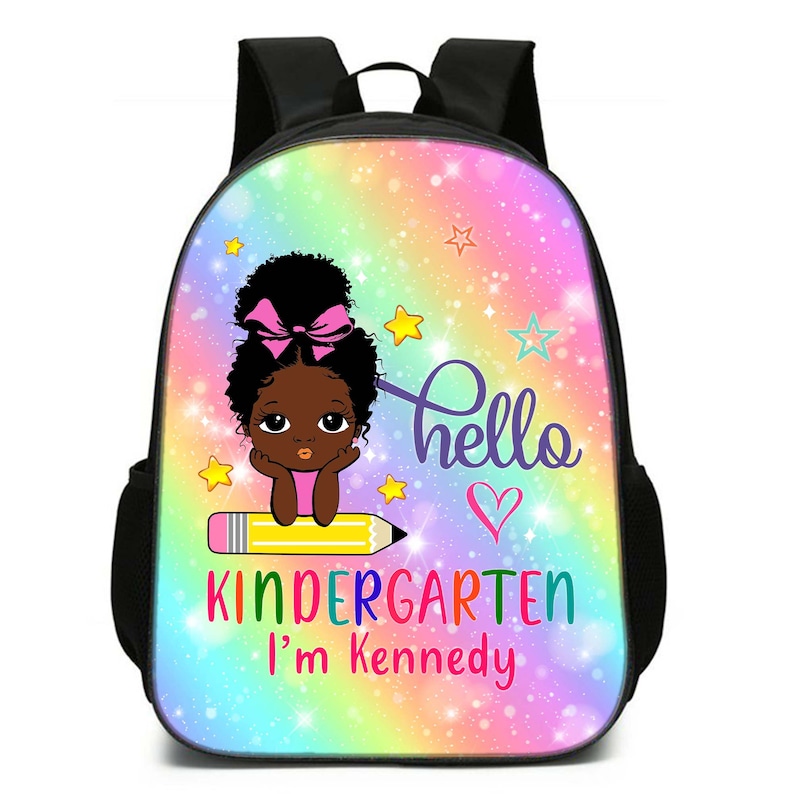 Peut inclure: Un sac &agrave; dos noir et rose avec un fond arc-en-ciel. Il repr&eacute;sente une fille de dessin anim&eacute; avec un n&oelig;ud rose et le texte "hello kindergarten I'm kennedy".