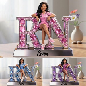 May include: A nurse figurine in a pink uniform sits on a large, jeweled "RN" emblem. The emblem is silver with pink gems. The name "Erica" is on the base. The image shows the figurine in three different colour schemes.