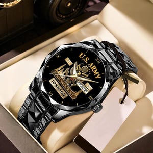May include: A black wristwatch with a faceted band and a black face. The watch face features the text "U.S. ARMY" and "250th Anniversary" with the name "JONHSON". The watch is presented in a beige box.