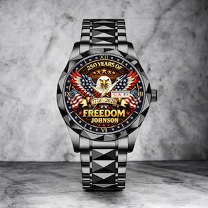 Puede incluir: Reloj de pulsera plateado con esfera detallada. La esfera presenta un &aacute;guila con las alas extendidas, banderas americanas y el texto "250 YEARS OF FREEDOM JOHNSON 1776-2026". La correa es de metal.