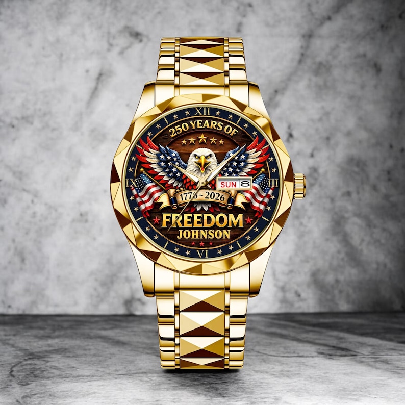 Puede incluir: Un reloj dorado con un dise&ntilde;o patri&oacute;tico. La esfera del reloj presenta un &aacute;guila, banderas americanas y el texto "250 Years of Freedom Johnson 1776-2026". La correa del reloj tiene un patr&oacute;n geom&eacute;trico.