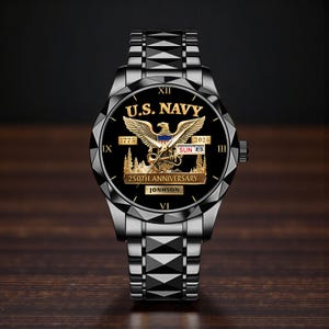 May include: A black wristwatch with a metallic band and a black face. The watch face features the text "U.S. NAVY" above a golden eagle emblem. The watch also displays the date and the text "250TH ANNIVERSARY".
