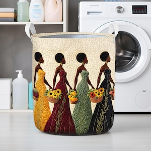 May include: A round laundry hamper featuring a design of four women in colorful gowns, each holding a basket of flowers. The women are depicted in profile against a quilted background. The hamper has white handles and a neutral color scheme.