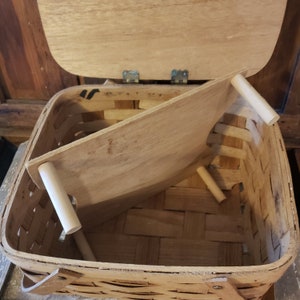 Puede incluir: Una cesta de picnic de madera con tapa con bisagras y una bandeja extra&iacute;ble. La cesta est&aacute; hecha de madera tejida y tiene un acabado natural. La bandeja tambi&eacute;n est&aacute; hecha de madera y tiene un acabado marr&oacute;n claro.