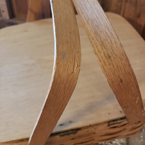 Puede incluir: Primer plano de las asas de madera de una cesta de picnic vintage. Las asas son de madera marr&oacute;n claro y tienen un aspecto ligeramente desgastado. La veta de la madera es visible y las asas est&aacute;n ligeramente curvadas.