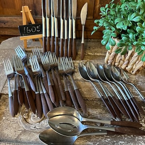 May include: A set of vintage silverware with brown wooden handles. The set includes forks, spoons, and knives. The silverware is arranged on a wooden surface.