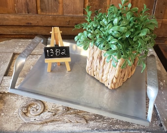 May include: A silver metal tray with two handles, a small wooden easel with a black chalkboard that says "1382", and a green plant in a woven basket.