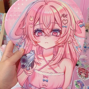 May include: Pink anime-style mousepad with a girl holding a gun. The girl has pink hair, red eyes, and is wearing a pink and white dress. The mousepad has a pink background with white stars and the word "PIPIPI" written on it.