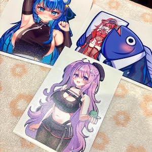 May include: Three rectangular stickers featuring anime-style characters. One shows a blue-haired character in a black top, another depicts a red-haired character with a large blue fish, and the third displays a purple-haired character holding a small green frog.