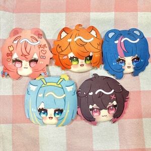 May include: Five circular acrylic charms featuring stylized anime-style character heads with distinct hair colors including pink, orange, blue, light blue, and dark purple. Each character has large expressive eyes, small mouths, and white wavy highlights.