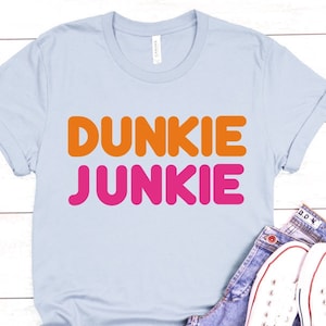 Puede incluir: Camiseta azul claro con el texto "Dunkie Junkie" en letras naranja y rosa.