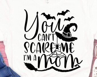 Può includere: T-shirt bianco con grafica nera che recita "You can't scare me I'm a Mom". Il design include pipistrelli, un cappello da strega, una ragnatela e una scopa. La maglietta è abbinata a jeans blu e scarpe da ginnastica bianche.