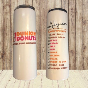 K&ouml;nnte beinhalten: Zwei wei&szlig;e Edelstahlbecher mit einem Dunkin' Donuts-Logo auf dem einen und einer Liste von Kaffeegeschmacksrichtungen und -optionen auf dem anderen. Der Becher rechts tr&auml;gt oben den Namen Alyssa.