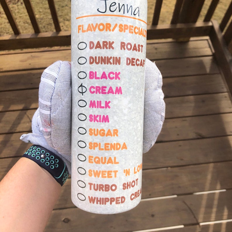 K&ouml;nnte beinhalten: Ein wei&szlig;er Becher mit einem schwarzen und orangen Design. Der Becher hat eine Liste von Kaffeeoptionen, darunter "Dark Roast", "Dunkin Decaf", "Black", "Cream", "Milk", "Skim", "Sugar", "Splenda", "Equal", "Sweet 'N Low", "Turbo Shot" und "Whipped Cream".