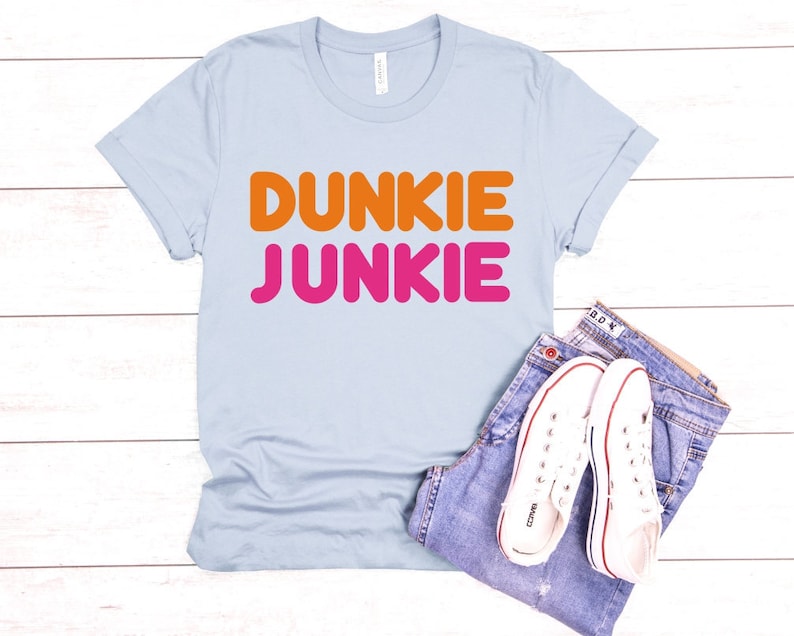 Puede incluir: Camiseta azul claro con el texto "Dunkie Junkie" en letras naranja y rosa.