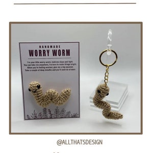 Puede incluir: Llavero de gusano de la preocupación hecho a mano de color beige. El llavero tiene una pequeña etiqueta con el texto "Handmade Worry Worm" y un mensaje sobre el uso del gusano para ayudar con la preocupación. La etiqueta está sobre un fondo blanco con un diseño floral.