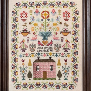 May include: Framed cross-stitch sampler featuring a house, floral motifs, birds, and the text "Jane Austen b. Dec 16.1775." The sampler is in a dark wooden frame, with a cream-colored background and colorful embroidery.