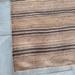 May include: A natural fiber rug with a striped pattern in shades of brown and black. The rug is woven with a textured, hand-crafted look.