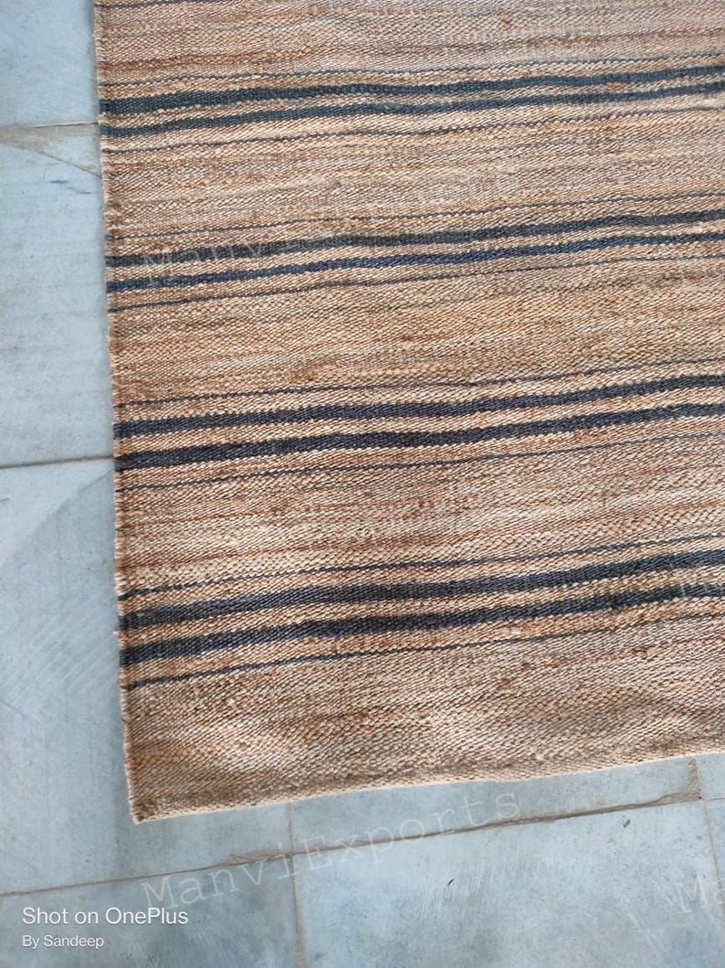 May include: A natural fiber rug with a striped pattern in shades of brown and black. The rug is woven with a textured, hand-crafted look.