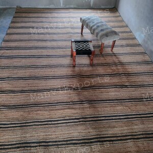 May include: A striped jute rug with black and natural colored stripes. Two wooden stools with patterned fabric cushions are placed on the rug. The rug is in a room with a window and white walls.