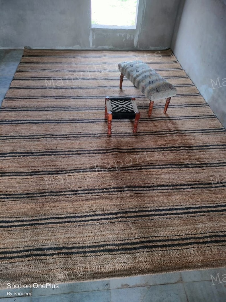 May include: A striped jute rug with black and natural colored stripes. Two wooden stools with patterned fabric cushions are placed on the rug. The rug is in a room with a window and white walls.