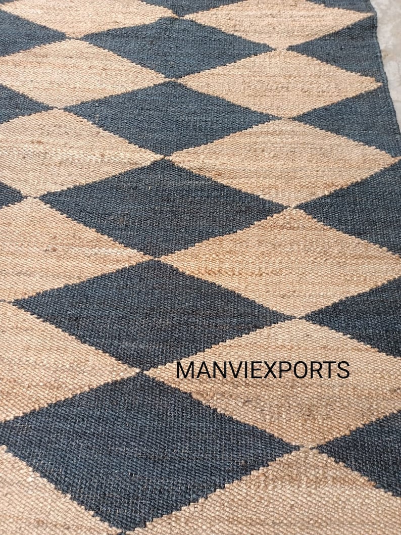 May include: A black and beige jute rug with a diamond pattern. The rug is woven with natural fibers and has a rustic look. The text "MANVIEXPORTS" is visible in the lower right corner of the rug.