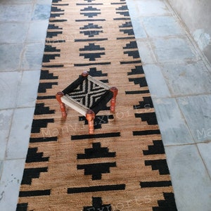 May include: A black and brown jute rug with a geometric pattern. The rug is laid out on a tiled floor with a small wooden stool in the center.
