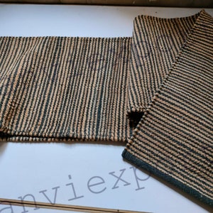 May include: A brown and black striped rug with a woven texture. The rug is folded in half and is lying on a white surface.