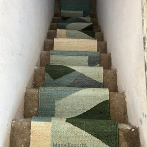 Może przedstawiać: Zestaw stopni schodowych z geometrycznym wzorem w odcieniach zieleni, błękitu i beżu. Stopnie wykonane są z naturalnego materiału włóknistego, takiego jak juta lub sizal. Stopnie są ułożone na schodach w domu.