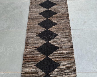 May include: A black and brown jute rug with a geometric diamond pattern. The rug is woven with a natural fiber and has a fringed edge.