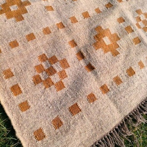 May include: Beige and brown woven rug with a geometric pattern. The rug features a repeating design of brown squares and cross-like shapes. The edges have a fringe detail.