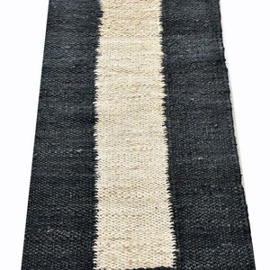 May include: A rectangular rug with a central cream-colored stripe flanked by black stripes. The rug has a woven texture and is likely made of natural fibers. This rug is suitable for home decor.
