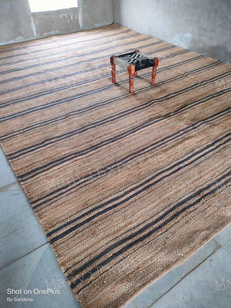 May include: A natural fiber rug with black and brown stripes. The rug is made of jute and is perfect for adding a touch of natural beauty to any room.