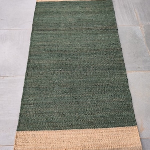 May include: A green and natural jute rug with a woven texture. The rug has a dark green centre and a natural jute border.