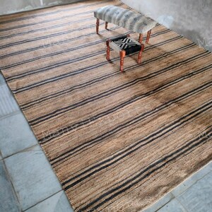 May include: A striped jute rug with black and natural brown stripes. Two small wooden stools with fabric cushions are on the rug. One stool has a black and white geometric pattern and the other has a white and gray pattern.