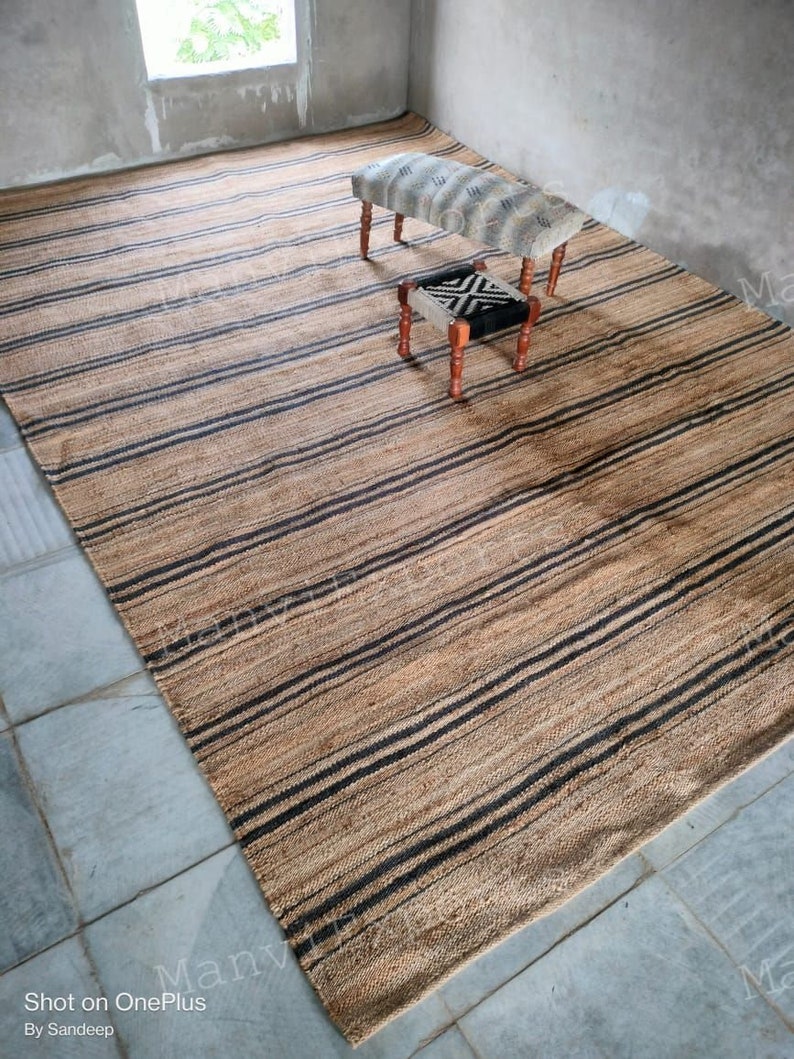 May include: A striped jute rug with black and natural brown stripes. Two small wooden stools with fabric cushions are on the rug. One stool has a black and white geometric pattern and the other has a white and gray pattern.